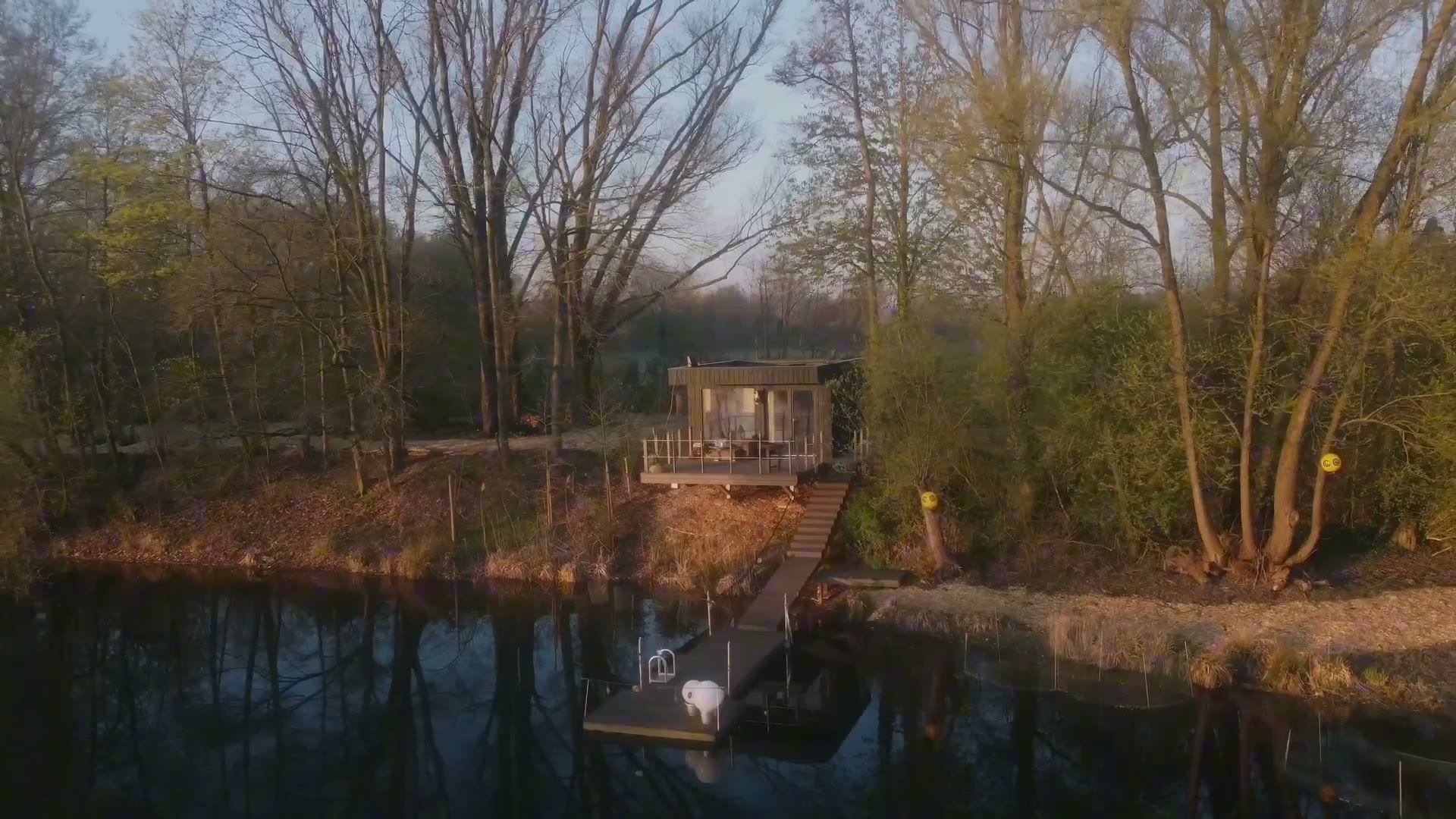 A wooden walkway leading to a dining deck on a still lake, sheltered by a parasol.